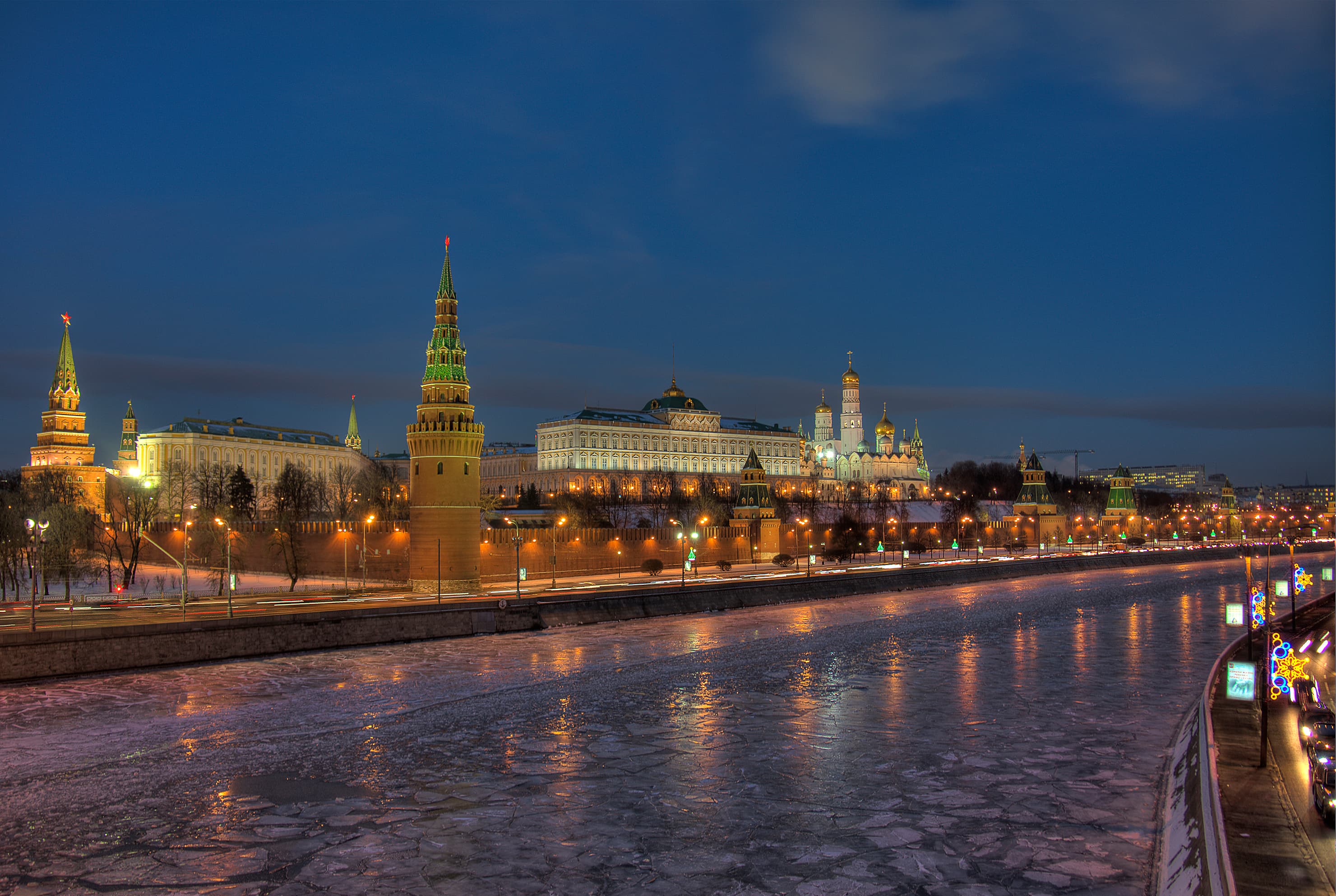 Kremlin de Moscou à noite, visto do outro lado do rio Moscou congelado, com as torres da muralha e o Grande Palácio do Kremlin iluminados.