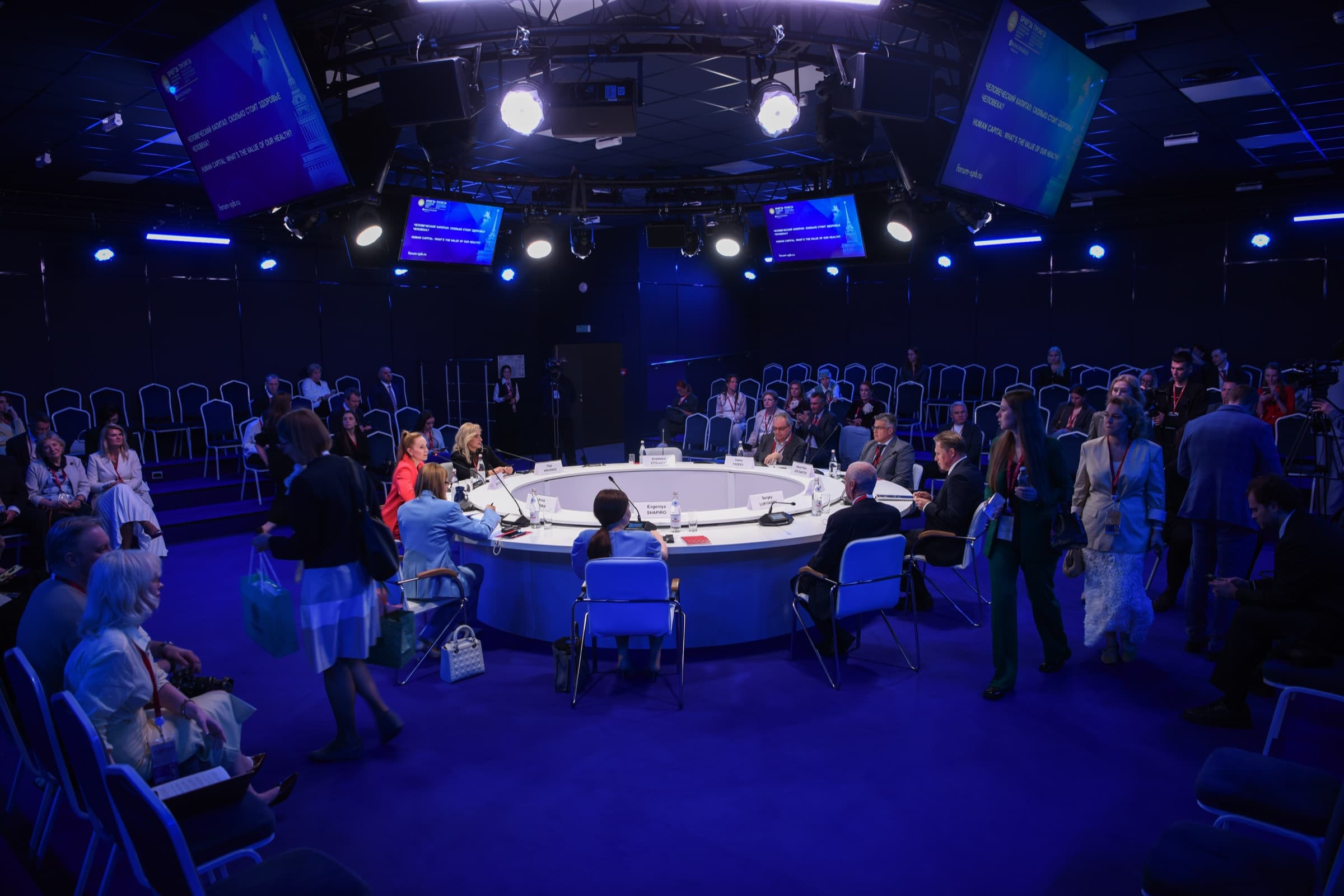 Mesa-redonda do SPIEF 2026 vista de cima, com participantes sentados em torno de uma mesa circular branca e telas exibindo o título da sessão sobre capital humano e saúde.