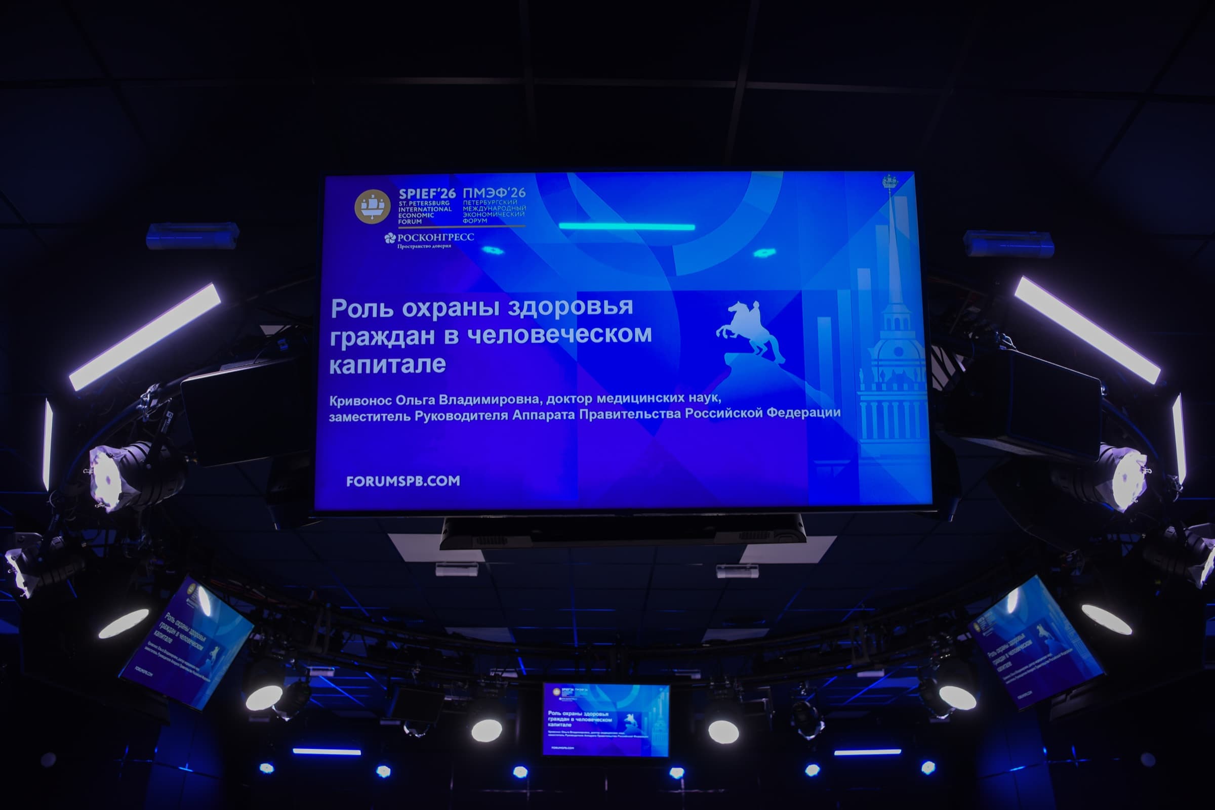 Telão suspenso na sala da sessão exibindo a marca do SPIEF 2026 e o título de uma apresentação sobre o papel da proteção à saúde no capital humano.